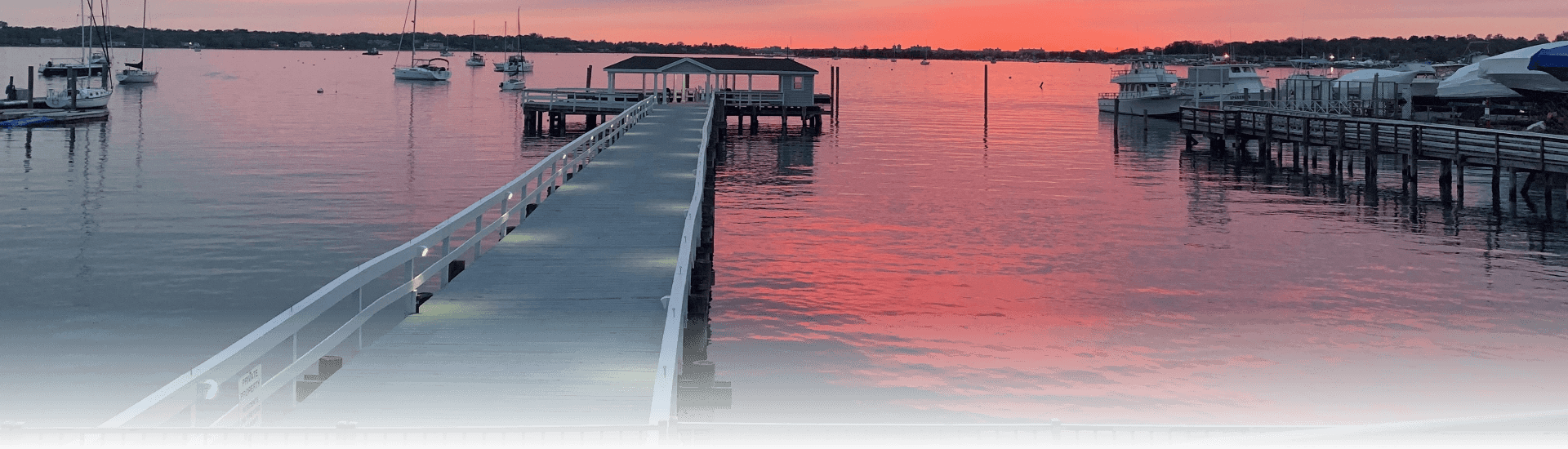 A pair of docs on a body of water with a number of boats at sunset with a number of boats