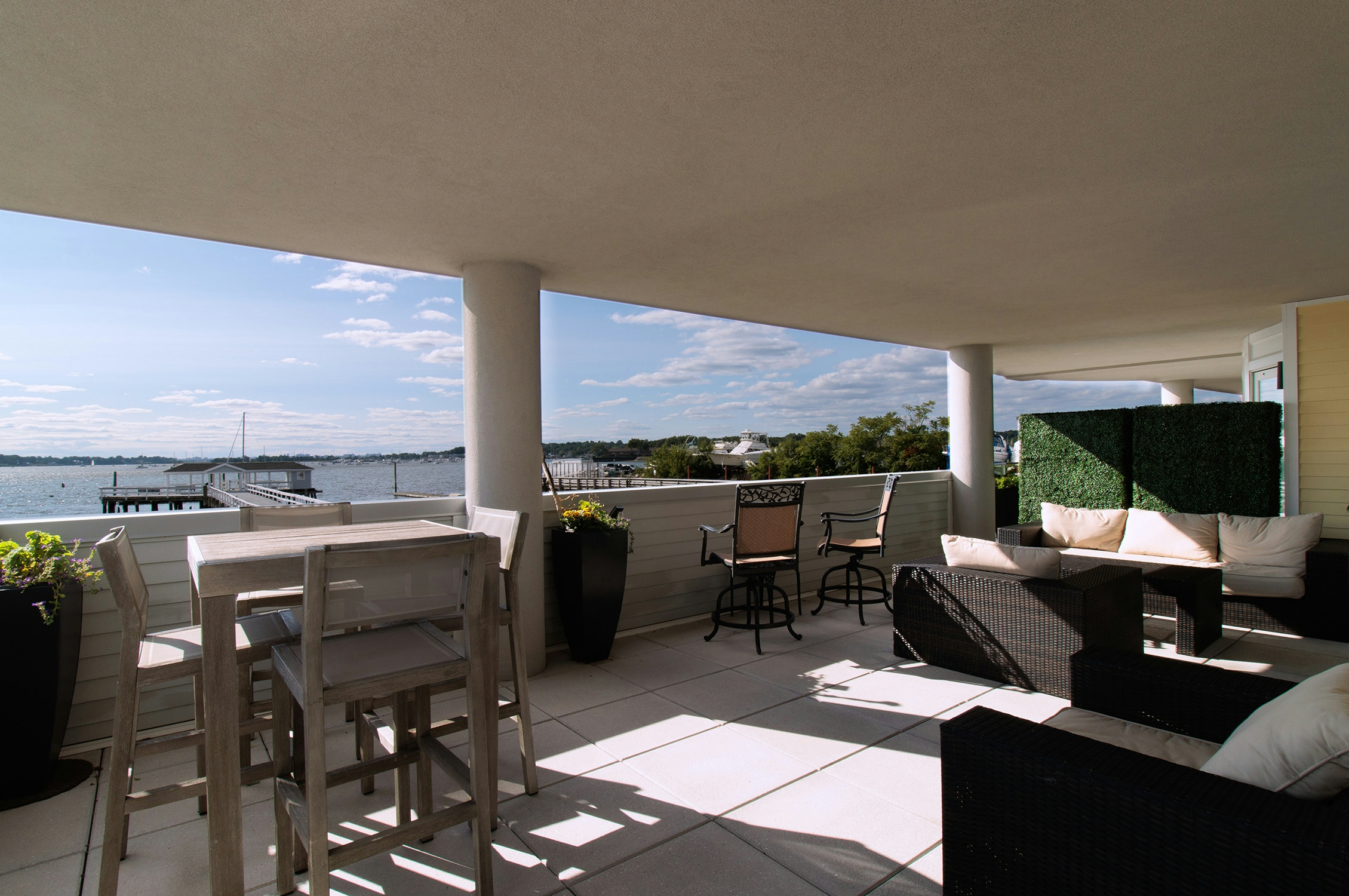 An outside terrace, with a wood table and 4 chairs, a sofa with cushions, and a view of Manhasset Bay