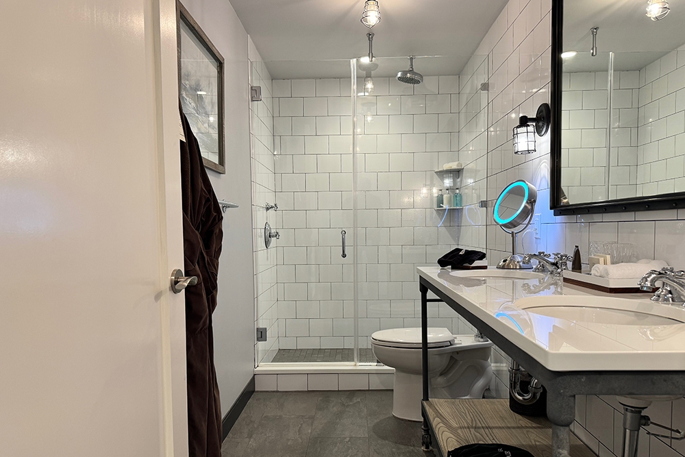 A bathroom with a double sink vanity, and a shower with clear glass shower doors.