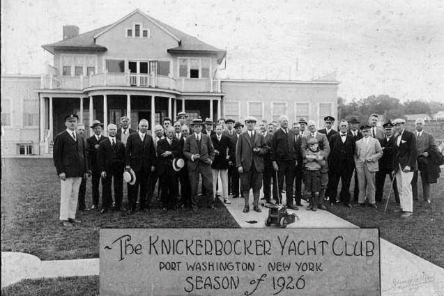 A black and white historic photo of a group of men and a boy in front of a prestigious building