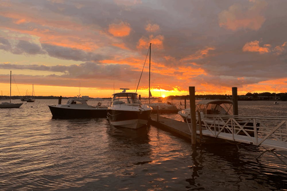 boats in the water by a dock with an orange and pink sunset
