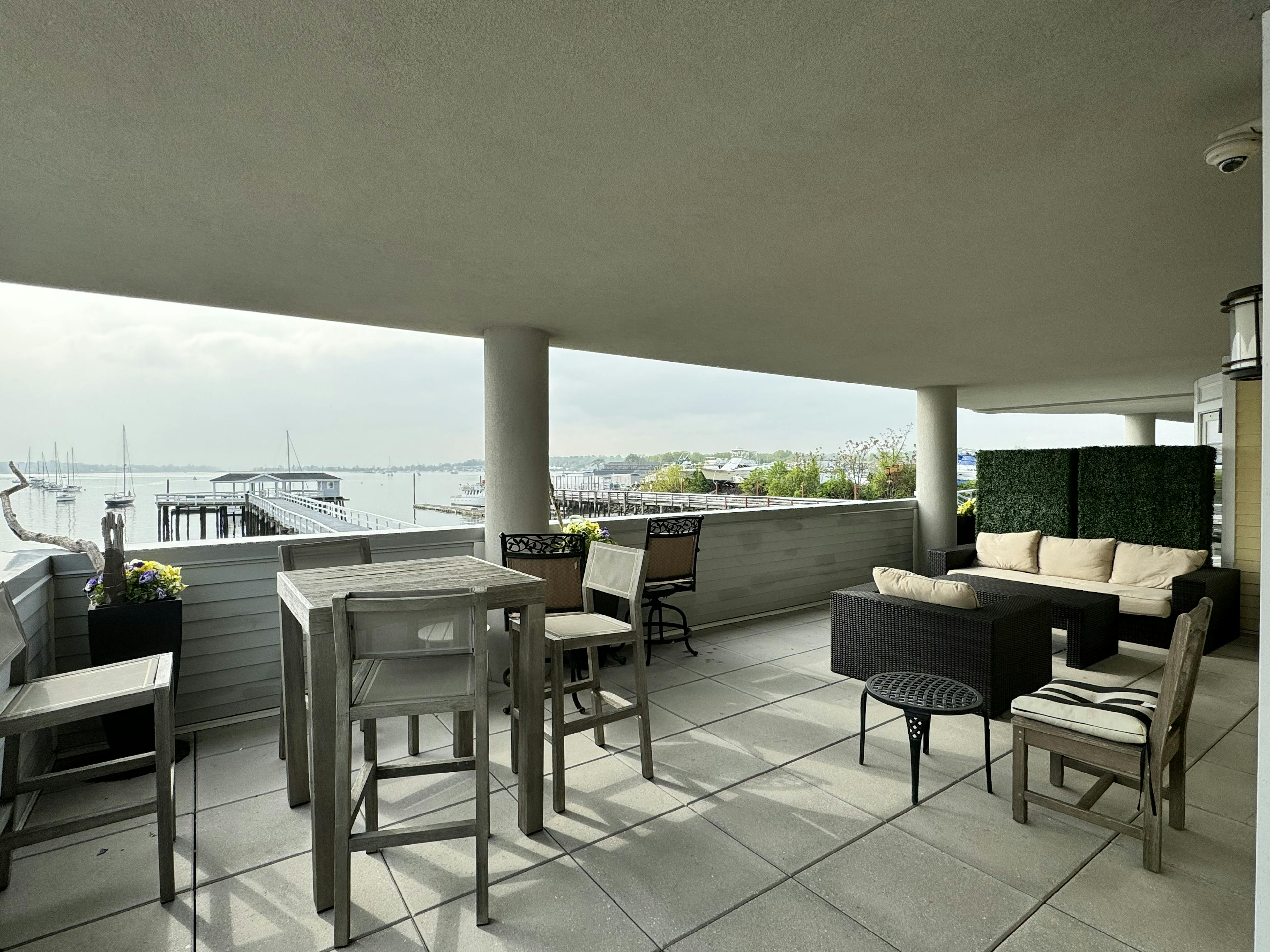 An outside terrace, with a wood table and 4 chairs, a sofa with cushions, and a view of Manhasset Bay