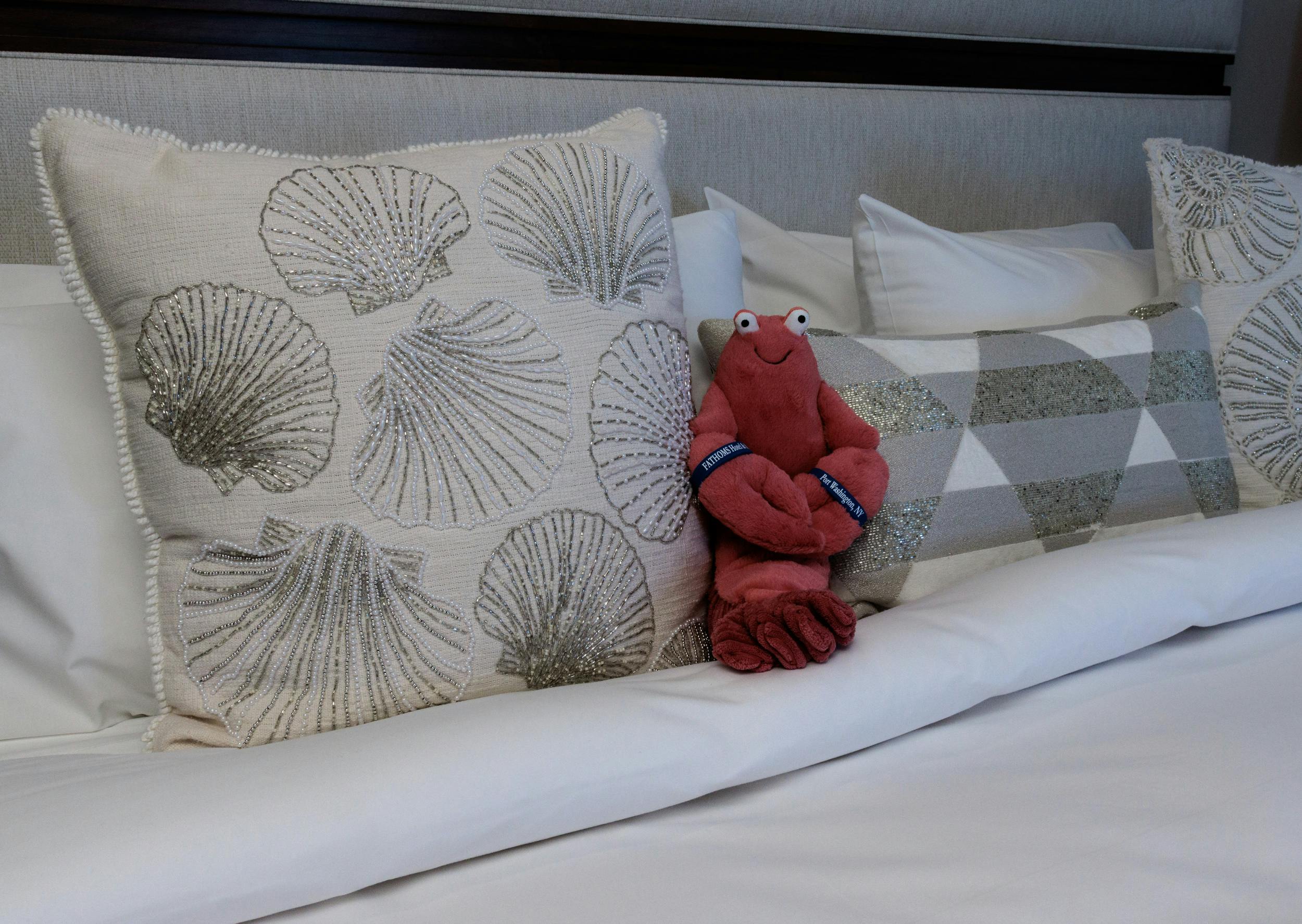 A closeup of bedding showing decorative pillows and a small red lobster plush stuffed animal toy.