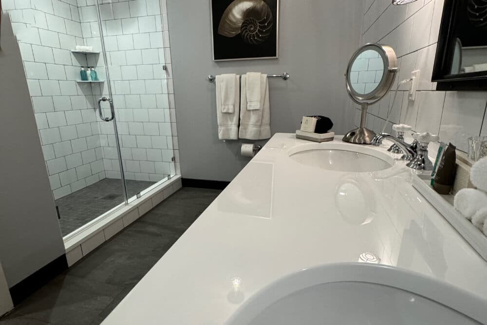 A bathroom with a double sink vanity, and a shower with clear glass shower doors.