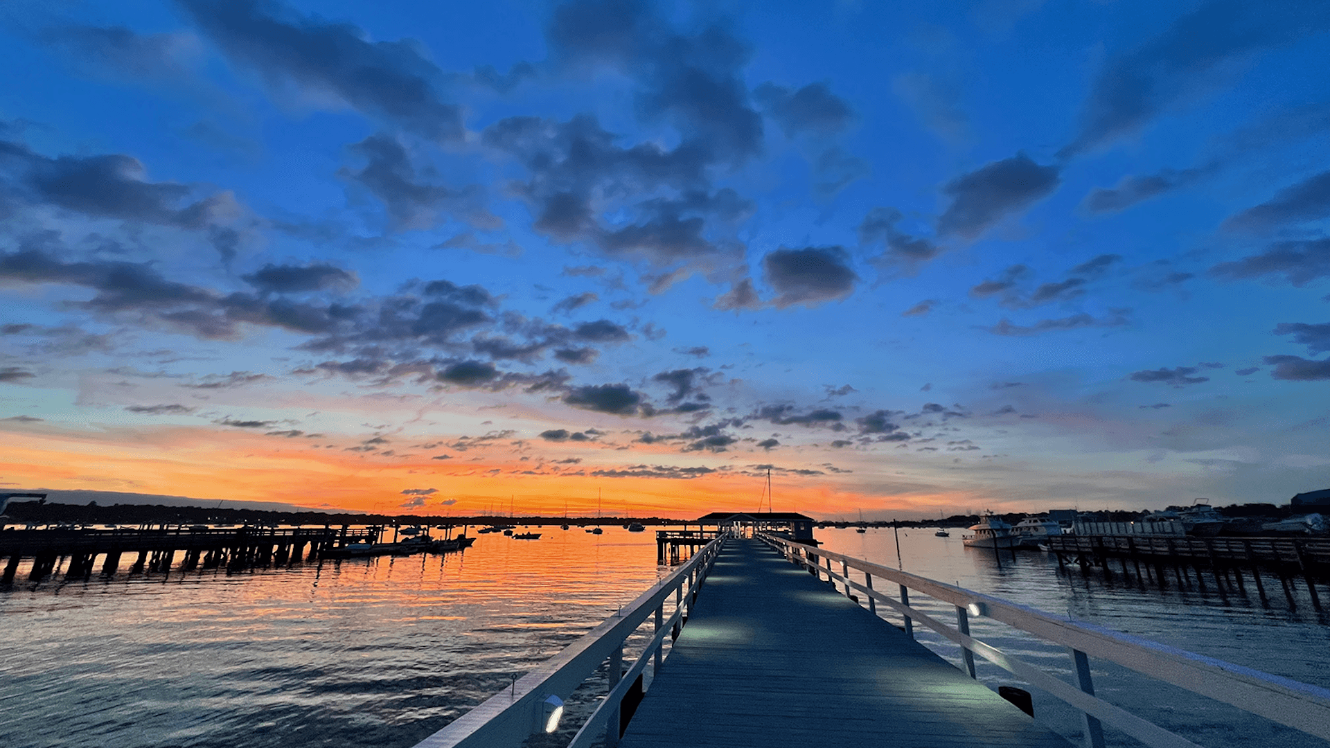 A pier extends into a tranquil body of water under a vibrant sunset sky filled with colorful clouds.