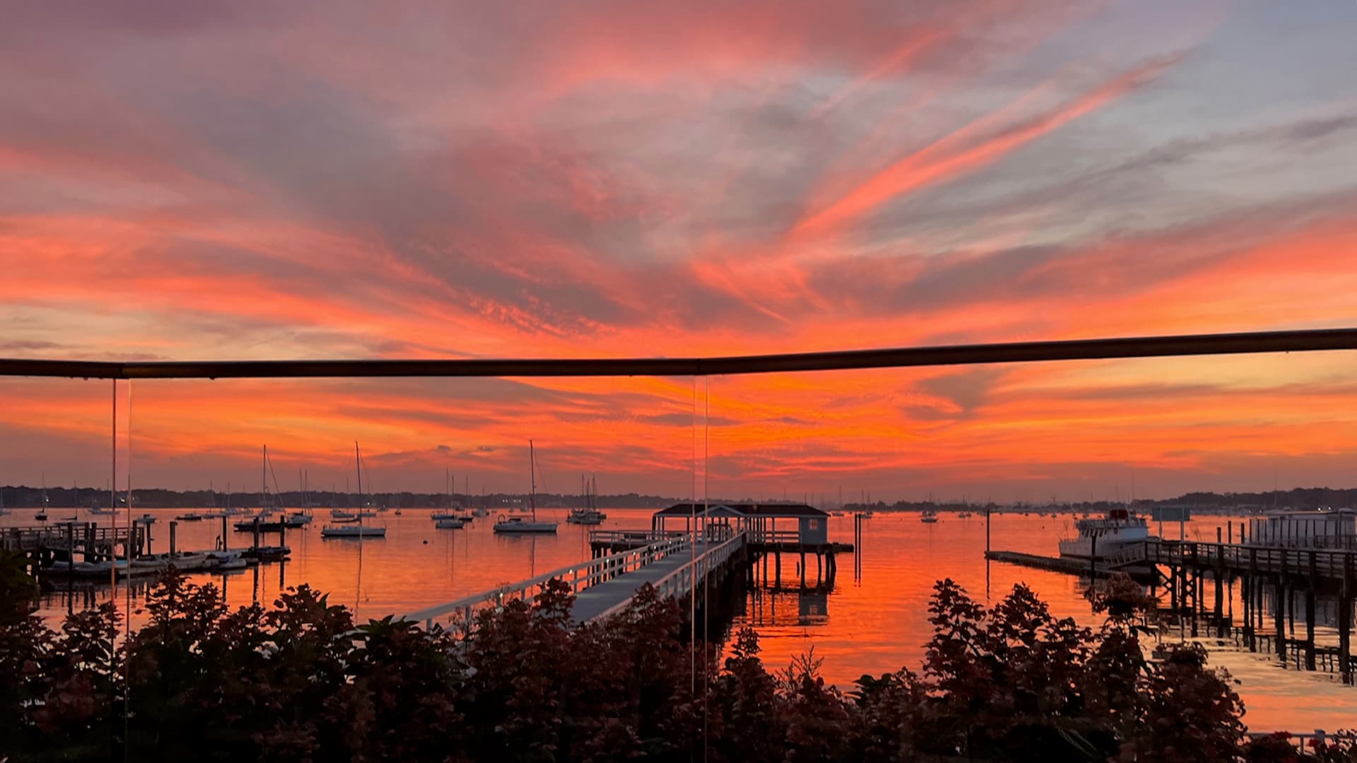 A vibrant sunset over a calm harbor, with silhouetted boats and piers.